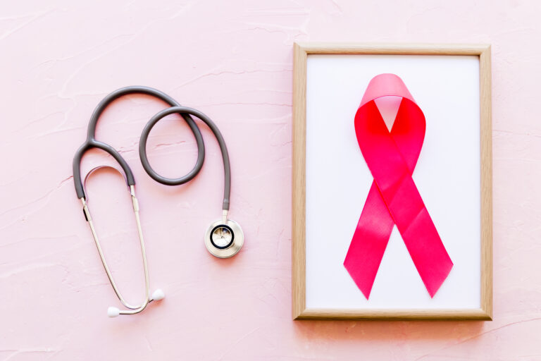 Stethoscope placed beside a wooden frame with a pink ribbon symbolizing breast cancer awareness and healthcare support